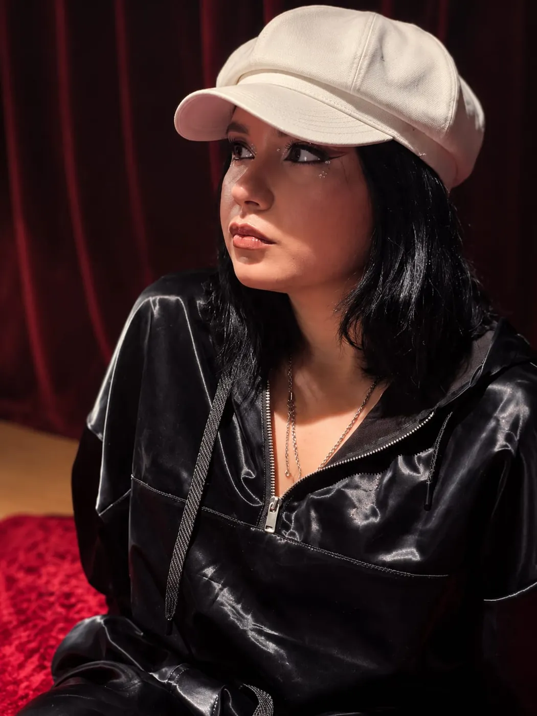 Dannery con gorra blanca y chaqueta negra, sentada frente a una cortina roja
